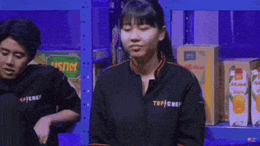 a woman wearing a black top chef shirt sits next to a man