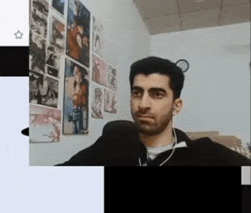 a man with a beard is sitting in front of a microphone in a room with posters on the wall .