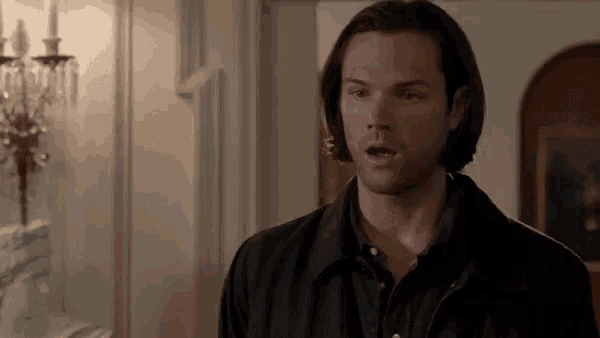 a man in a black jacket is standing in a room with his mouth open and a surprised look on his face .