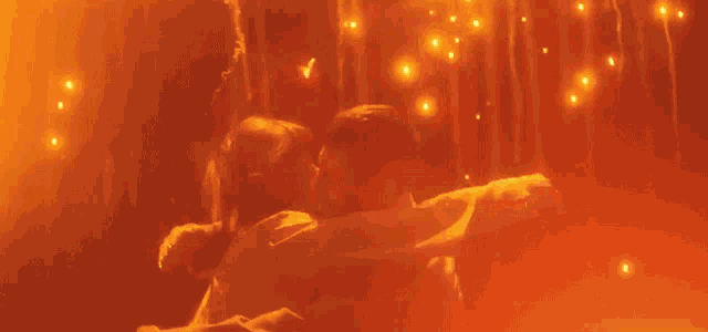 a man and woman are kissing in front of a glowing orange background