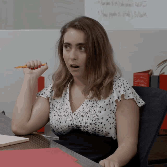 a woman sitting at a desk holding a pencil in her hand