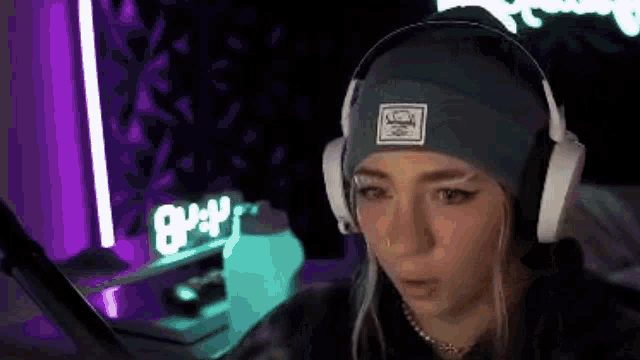 a woman wearing headphones and a beanie is sitting in front of a computer .