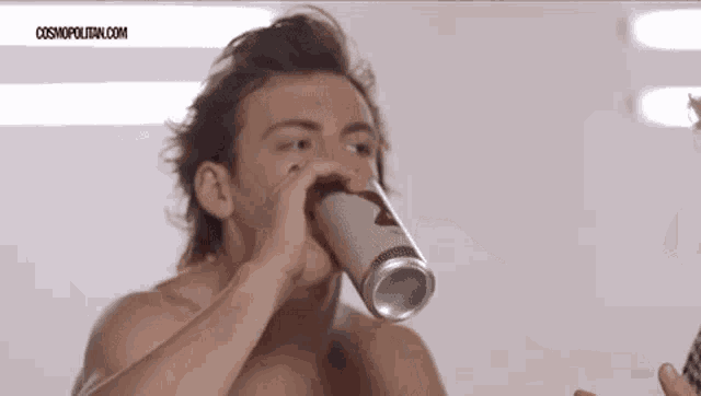 a shirtless man is drinking from a can with the website cosmopolitan.com written on the bottom