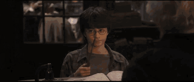 harry potter is sitting at a table in a dark room looking at something