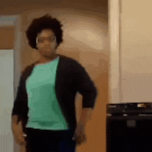 a woman in a green shirt and black sweater is standing in a room .