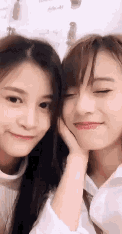 two girls are touching their faces and smiling at the camera .