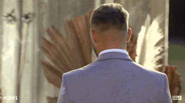 a man in a suit is standing in front of a wall with # mafs written on the bottom right