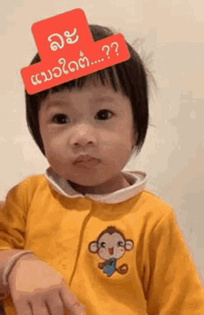 a little girl wearing a yellow jacket with a monkey embroidered on it is making a funny face .