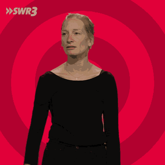 a woman in a black shirt stands in front of a red circle with swr3 in white letters