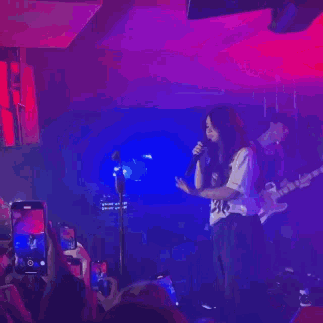 a woman is singing into a microphone on a stage while people take pictures with their phones .
