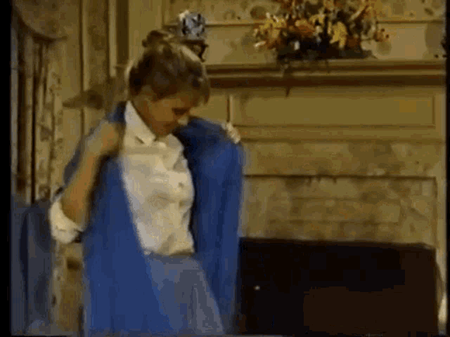 a woman is standing in front of a fireplace wearing a blue jacket and white shirt .