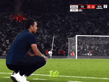 a man squatting on a soccer field with a score of gs 0 5 and bjk 44