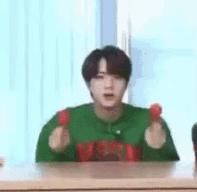 a man in a green sweater is sitting at a table holding two red balls .