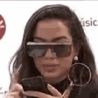 a woman wearing sunglasses and earrings is holding a cell phone .