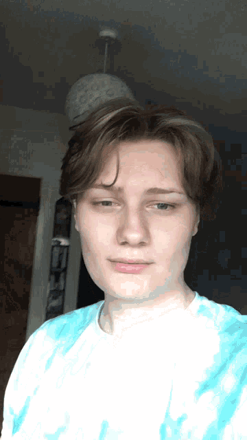 a young man wearing a blue tie dye shirt is taking a selfie