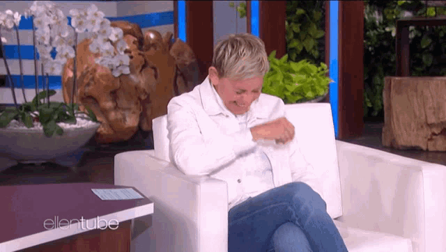 a woman in a white jacket is sitting in a chair in front of a table that says ellentube on it