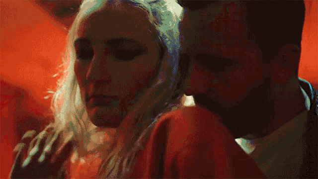 a man and a woman are hugging each other in a dark room . the woman is wearing a red dress .