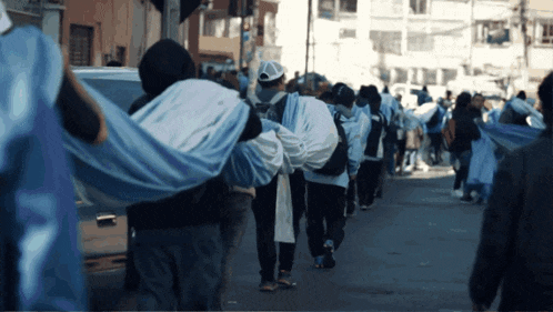 a group of people are walking down a street and one of them is wearing a white adidas shirt