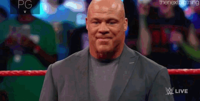 a bald man in a suit is standing in a wrestling ring and smiling .