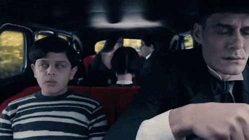 a boy in a striped sweater sits next to a man in a suit in a car