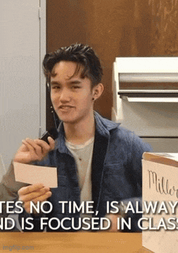a young man sitting at a table holding a piece of paper with the words " yes no time is always and is focused in class "