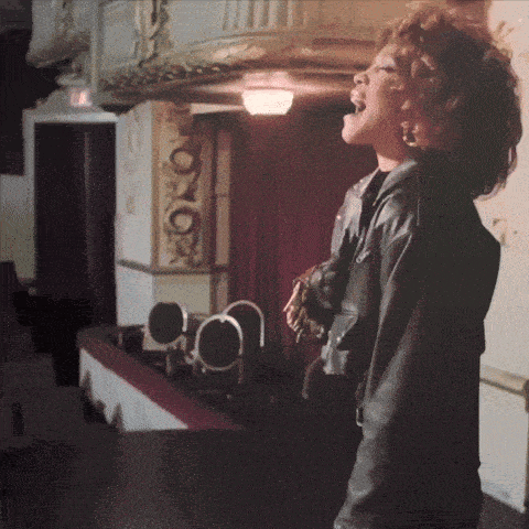 a woman in a black leather jacket is singing into a microphone on a stage