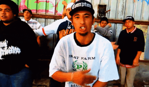 a man wearing a compton hat stands in front of a group of men