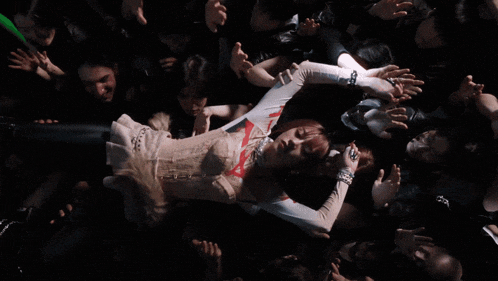 a woman in a white top is surrounded by a crowd of people with their hands out