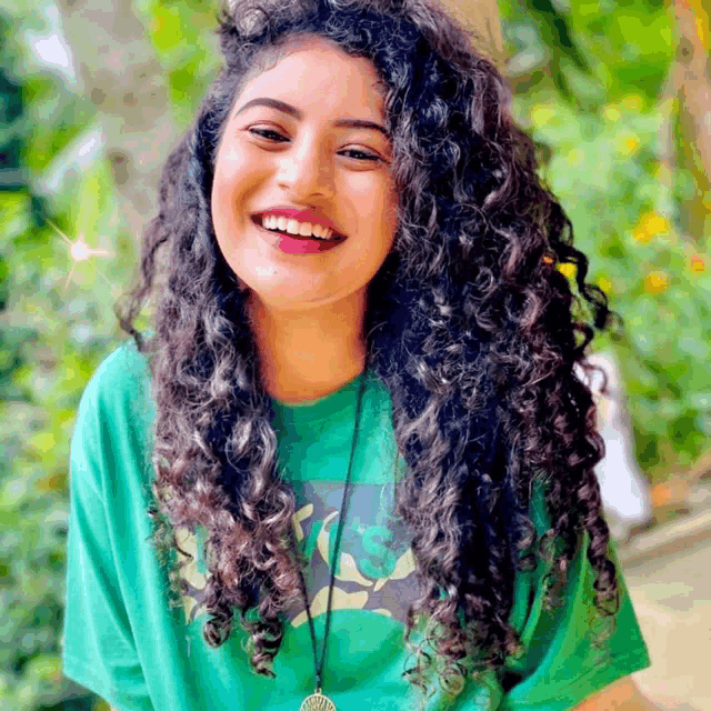 a woman with curly hair wearing a green shirt smiles