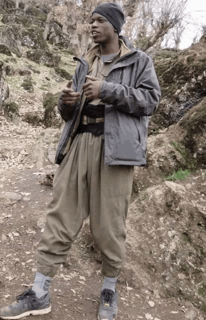 a man wearing a gray jacket and khaki pants is standing on a dirt path