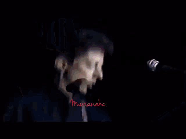 a man is playing an electric guitar in a dark room and the name marianahe is on the bottom right
