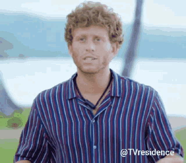 a man with curly hair is wearing a striped shirt and a necklace around his neck .