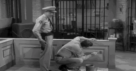 a black and white photo of two men in a jail cell painting a wall .