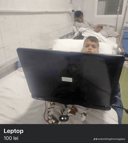 a boy is laying in a hospital bed using a laptop