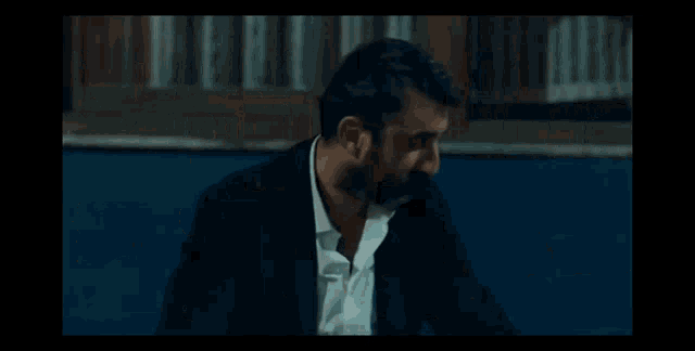 a man in a suit and white shirt is holding a gun in his hand in a dark room .