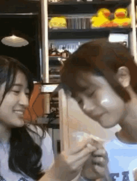 a girl is feeding a boy a piece of bread in front of a shelf with rubber ducks on it .