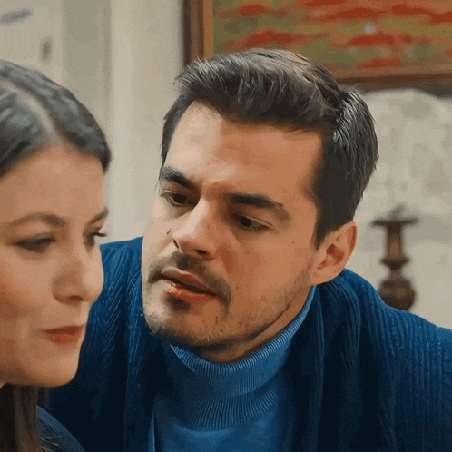 a man and woman are looking at each other and the man is wearing a blue turtleneck