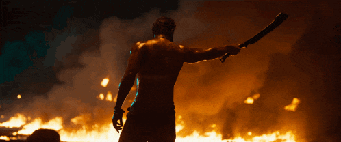 a shirtless man holding a sword in front of a fire