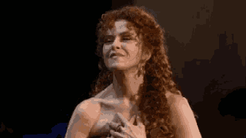 a woman with red curly hair is standing on a stage holding her chest .