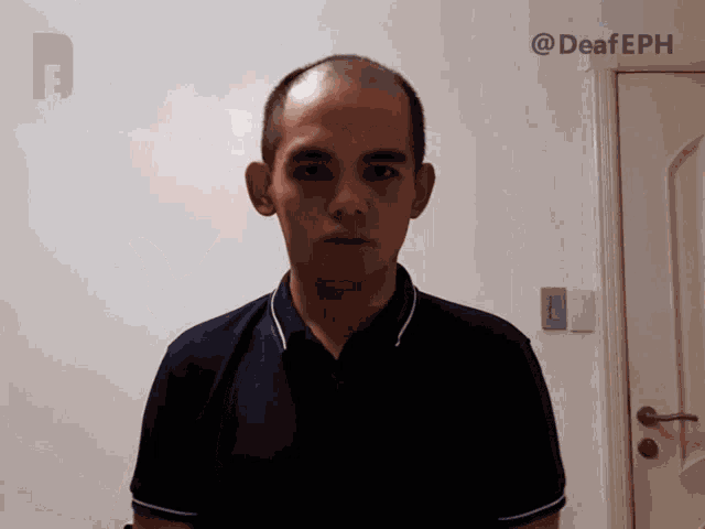 a man with a bald head stands in front of a white wall with the words @deafeph on it
