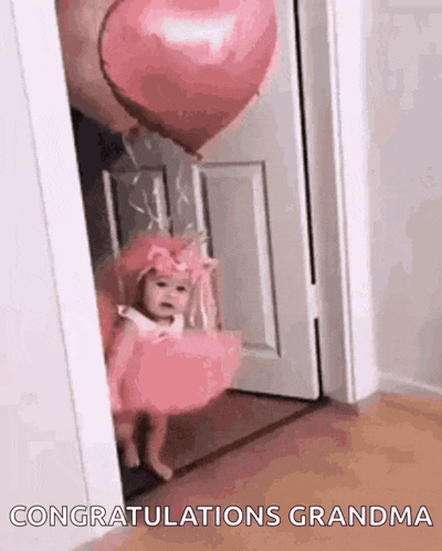 a little girl in a pink dress is standing in a doorway holding a pink heart shaped balloon .