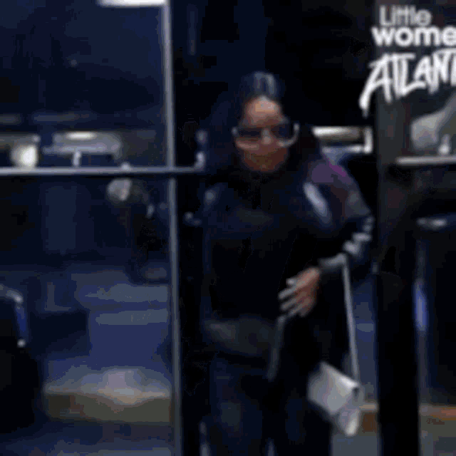 a woman wearing sunglasses and a little wome atlas shirt is walking down the street