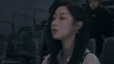 a woman with long black hair is sitting in a dark room looking at something .