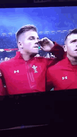 a man in a red under armour jacket wipes his nose with his hand
