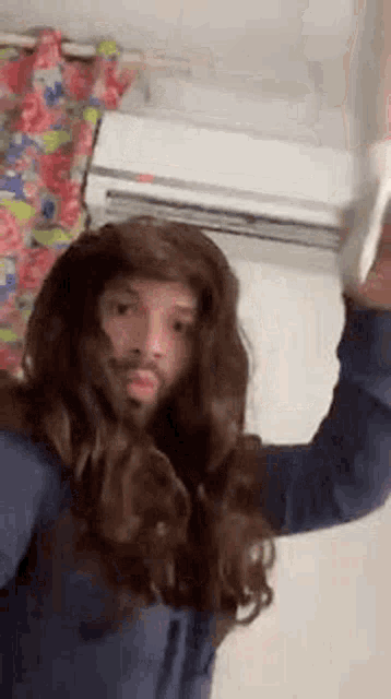 a man wearing a wig and a beard is standing in front of a wall air conditioner .