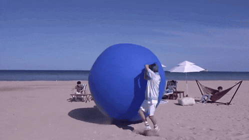 a group of people are playing with a large blue balloon on a beach