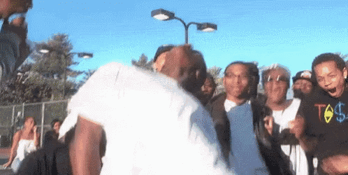 a group of people are standing around a man in a white shirt with a t on it .