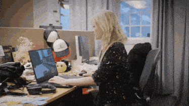 a woman sitting at a desk with a laptop and a hat that says ' a ' on it