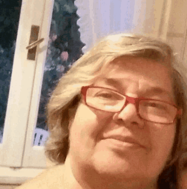 a woman wearing red glasses is taking a selfie .
