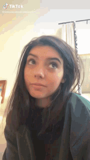 a girl with long dark hair is looking up at the camera while wearing a green sweatshirt .